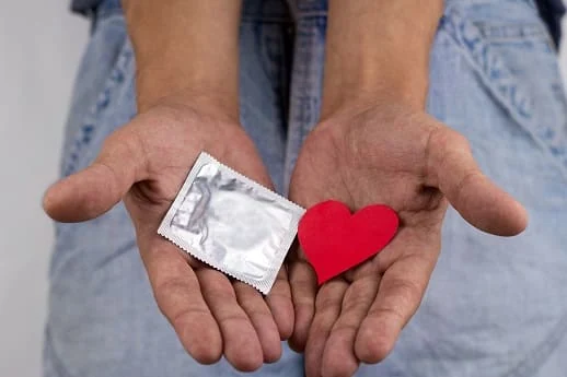 close up of male hands holding a condom pack and a red heart, safe sex concept