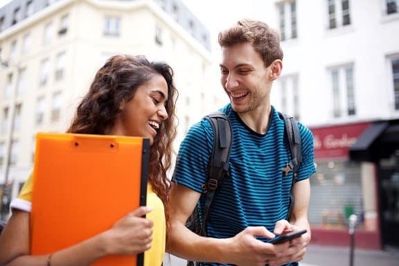 two happy college students walking in city looking at cellphone