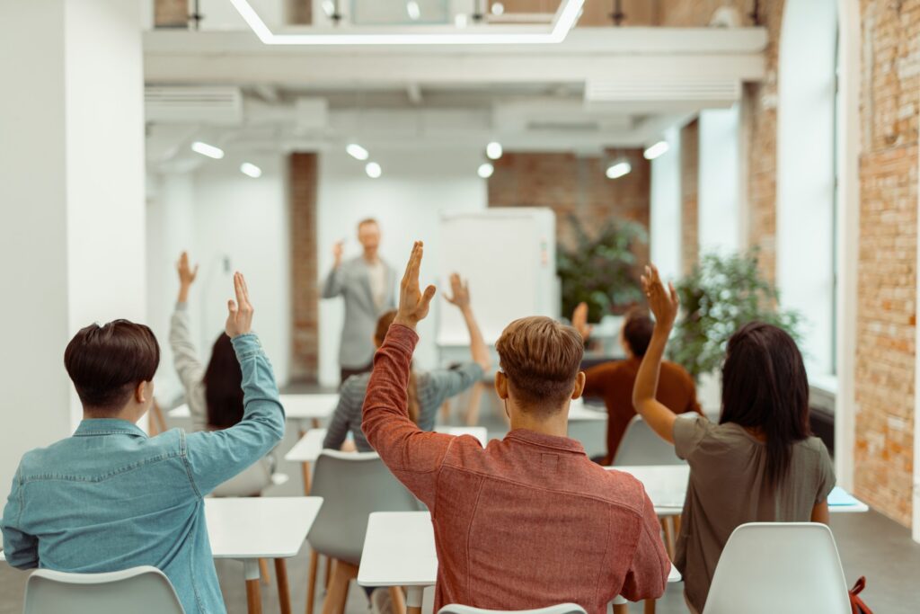 back view of students raising their hands during lecture in the classroom