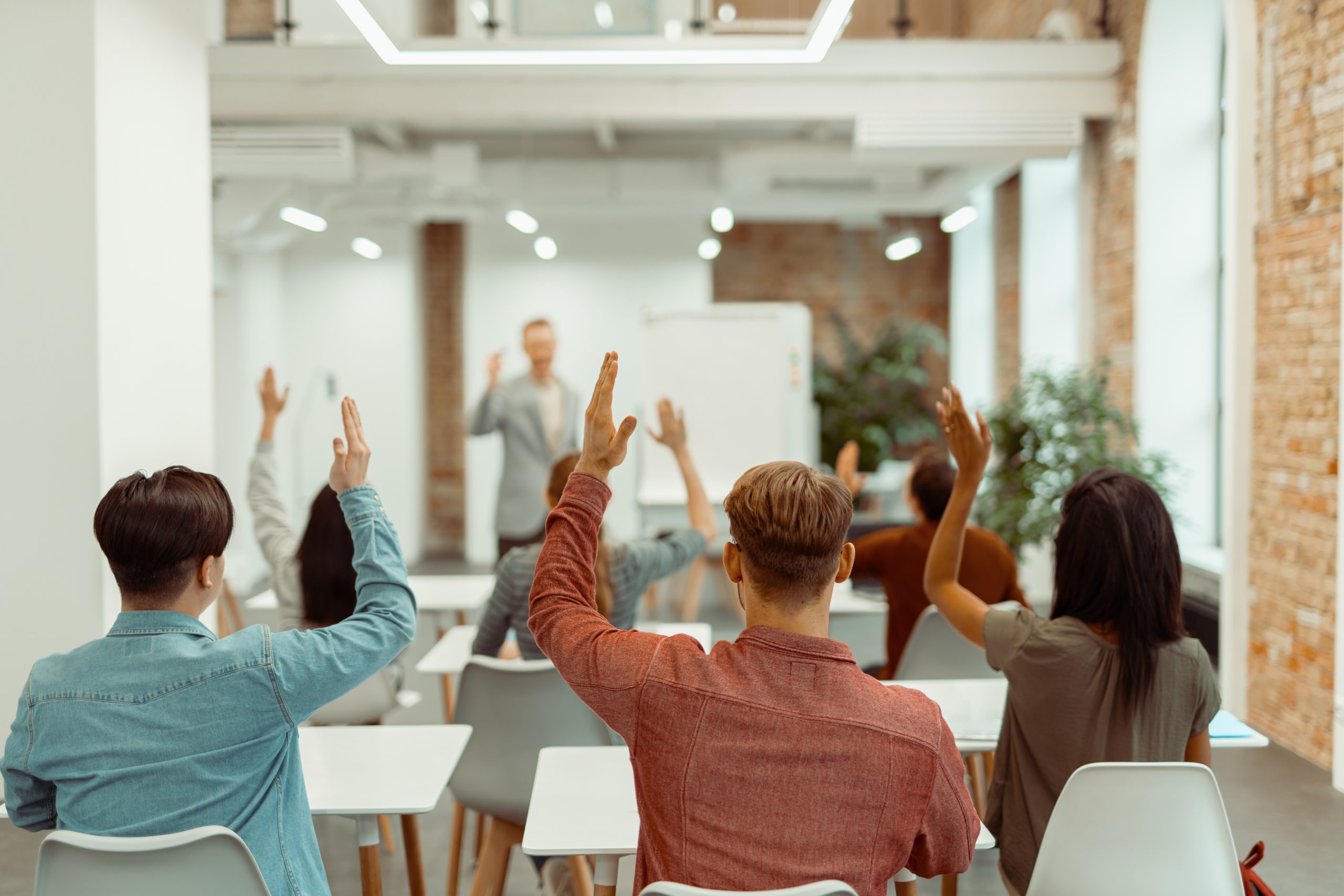 back view of students raising their hands during lecture in the classroom