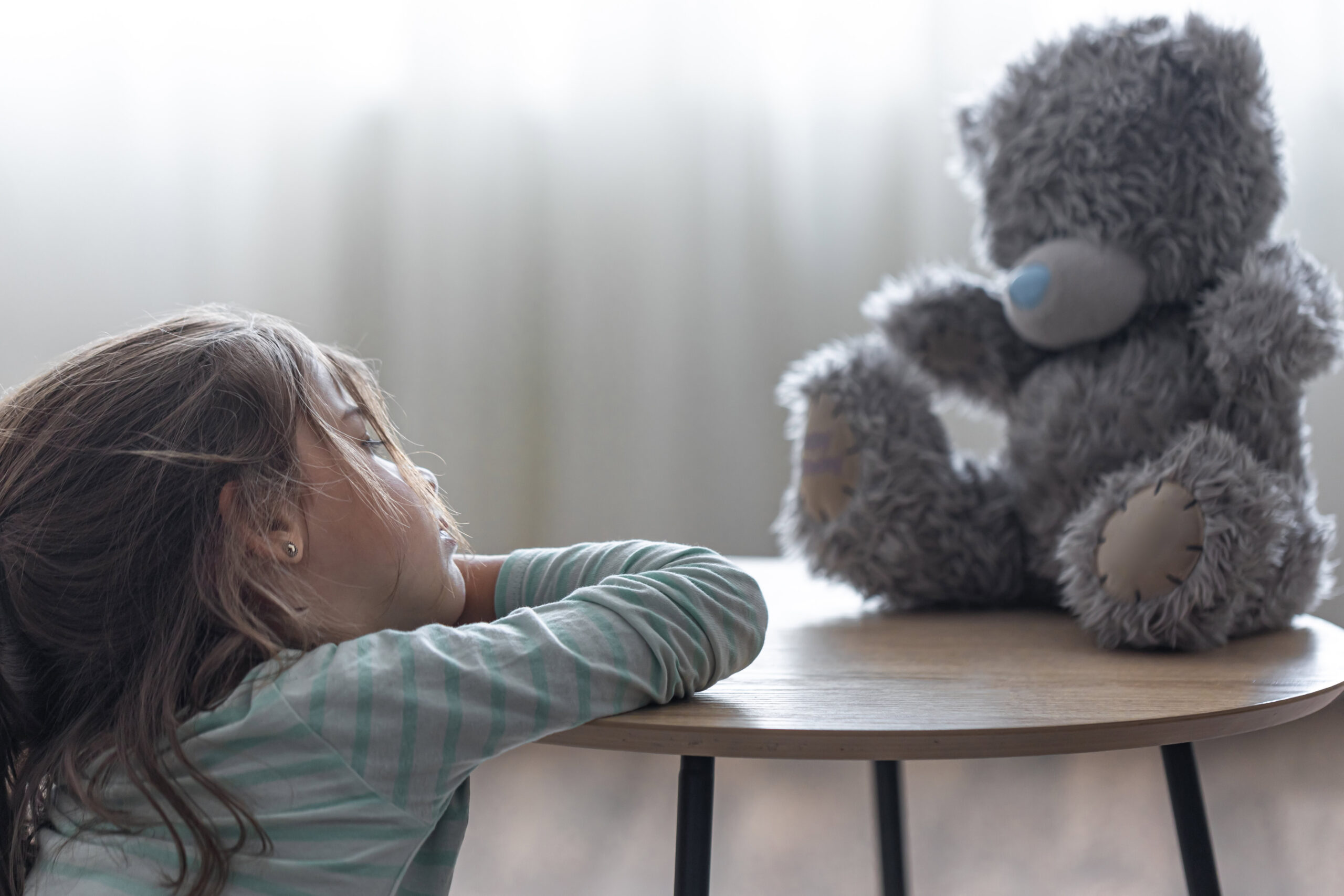 little girl looks her teddy bear child with favorite toy blurred background copy space